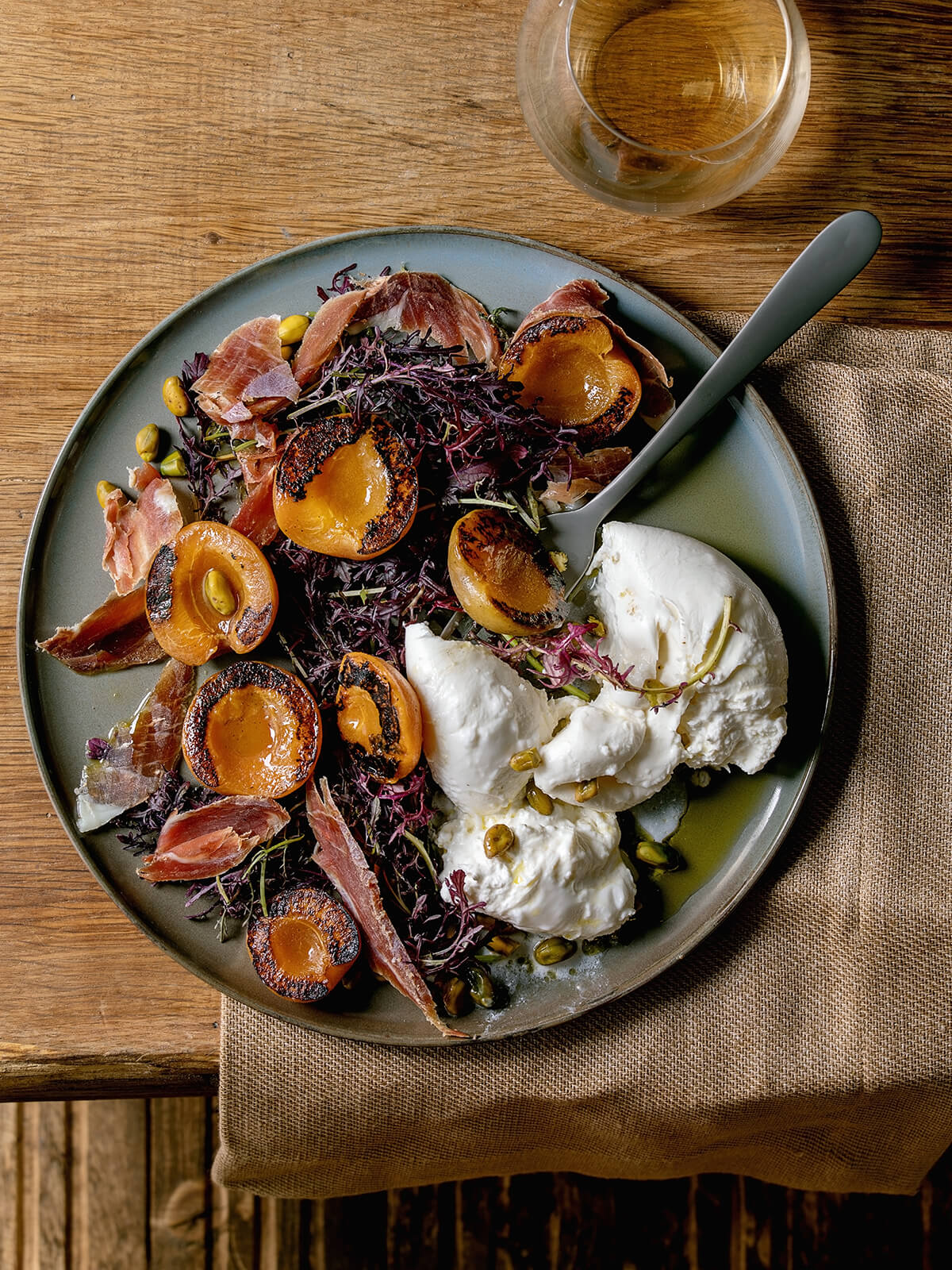 Burrata mit gegrillten Aprikosen, Prosciutto und rotem Senfsalat auf grauer Keramikplatte