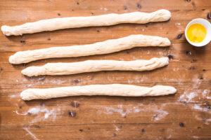Vier rohe Hefeteig-Stränge nebeneinander vor dem Flechten