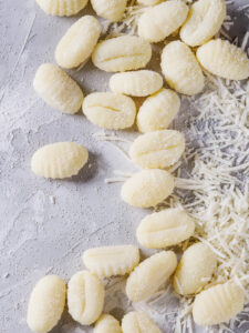 Rohe Kartoffel-Gnocchi mit Längskerbe und Gabelrillen neben geriebenem Parmesan auf hellem Stein