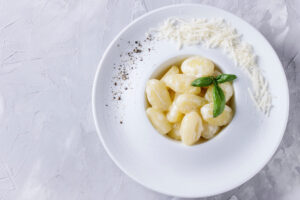 Cremige Kartoffel-Gnocchi in Sahne-Parmesan-Sauce von oben im weißen tiefen Teller, mit Parmesan und Pfeffer am Tellerrand und einem Basilikum-Zweig
