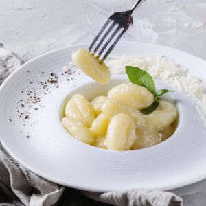 Cremige Kartoffel-Gnocchi in Sahne-Parmesan-Sauce im weißen tiefen Teller, eine Gnocchi auf der Gabel