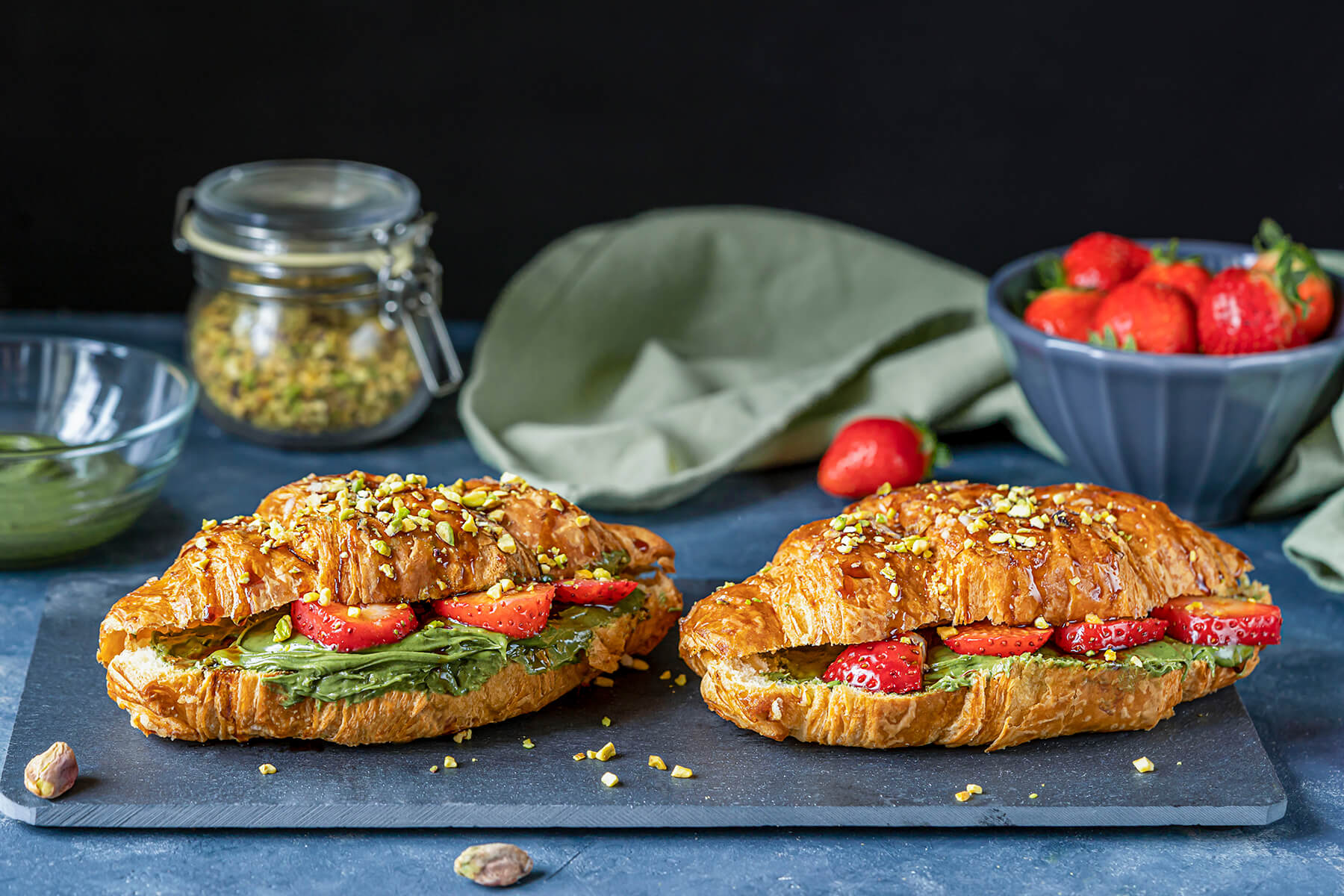Süße Croissant-Sandwiches mit Pistazien-Creme und Erdbeeren auf Holzbrett