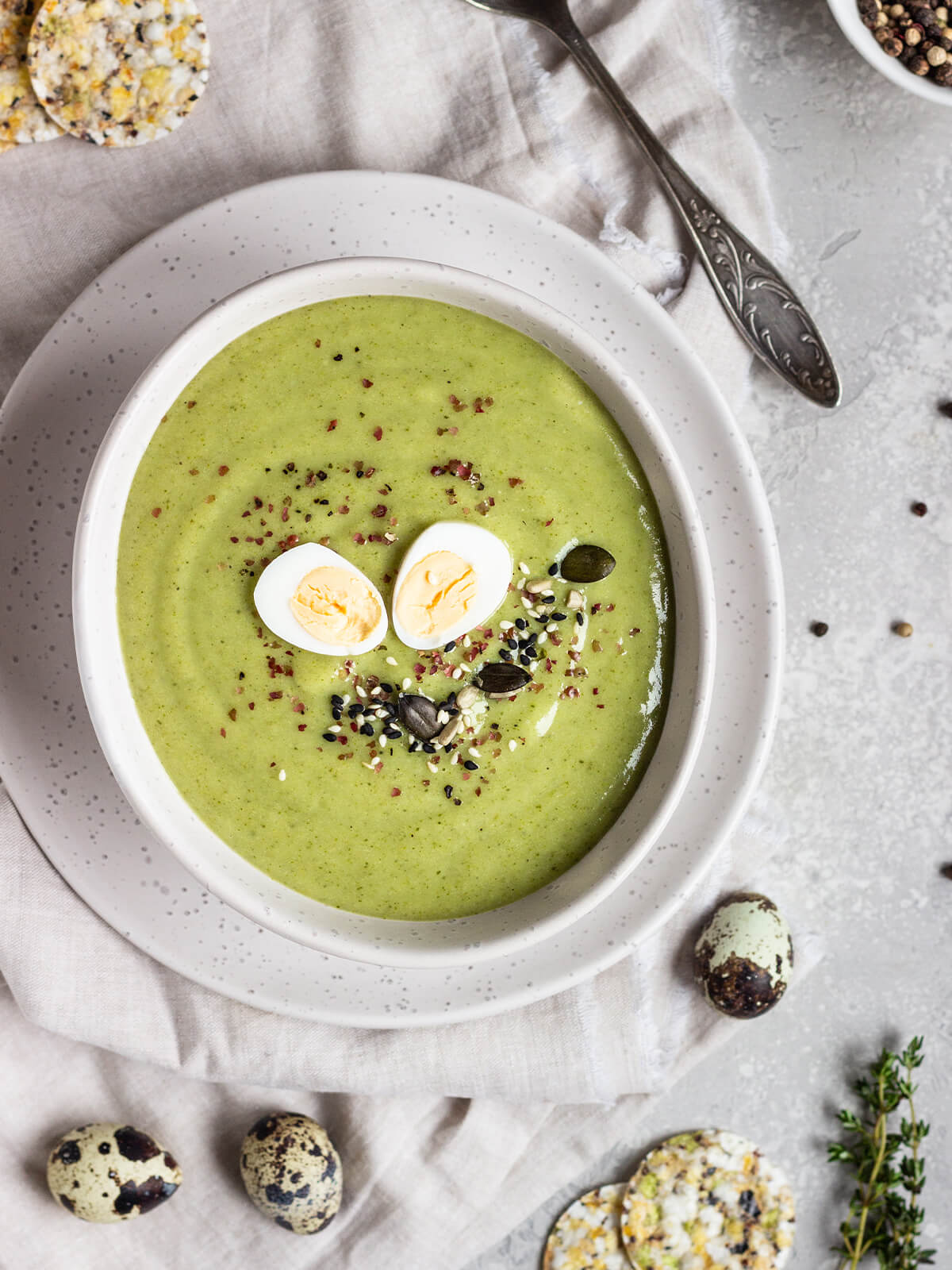 Grüne Brokkoli-Cremesuppe in heller Schale mit halbierten Wachteleiern, Sesam und Kürbiskernen, dekoriert mit Thymian