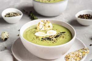 Schale grüne Brokkoli-Cremesuppe von der Seite mit halbierten Wachteleiern, Saatenmix und rosa Pfeffer