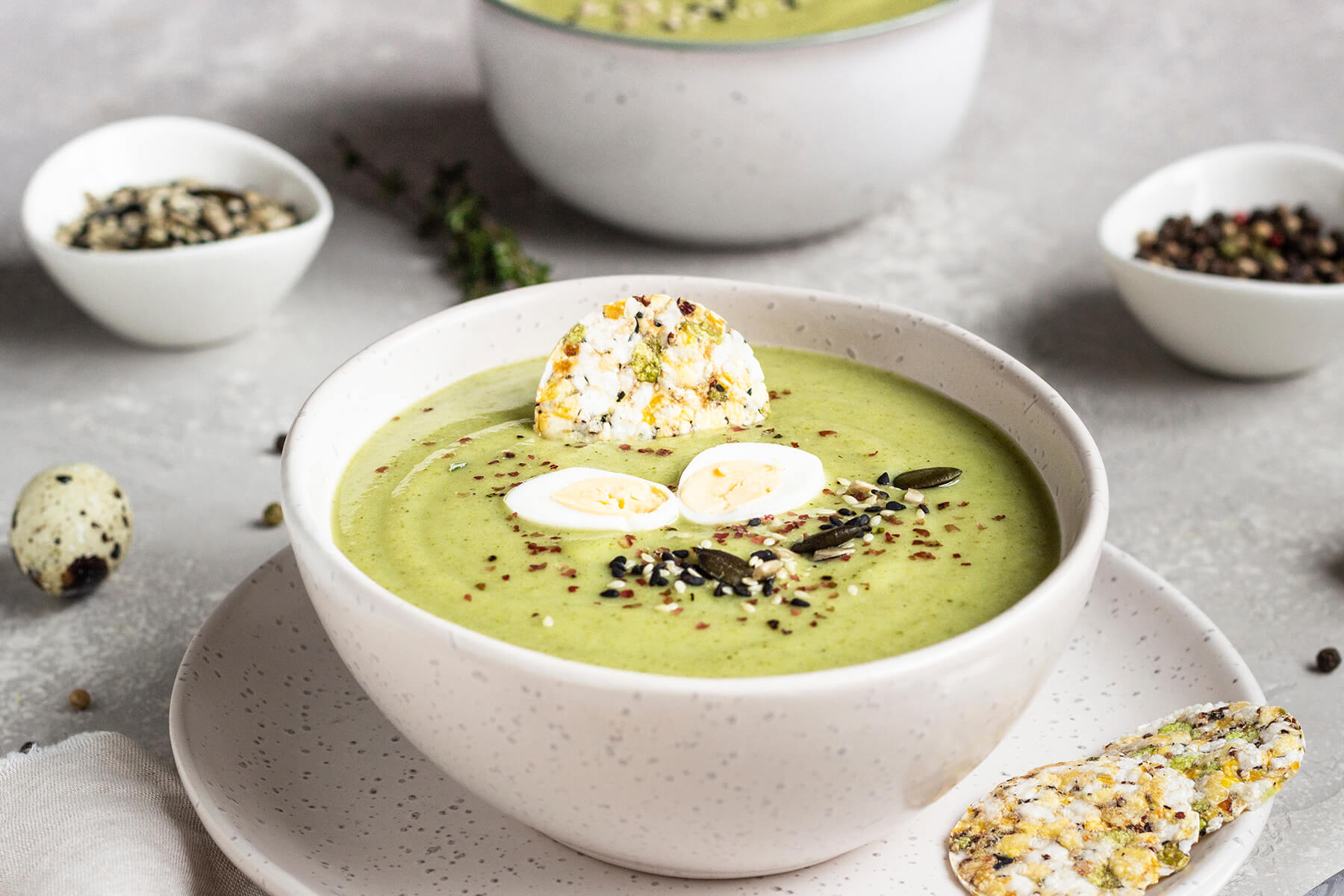 Schale grüne Brokkoli-Cremesuppe von der Seite mit halbierten Wachteleiern, Saatenmix und rosa Pfeffer
