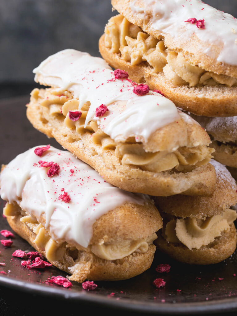 Nahaufnahme von Éclairs mit weißer Schokoladenglasur, gefriergetrockneten Himbeeren und cremiger Crème-Pâtissière-Füllung