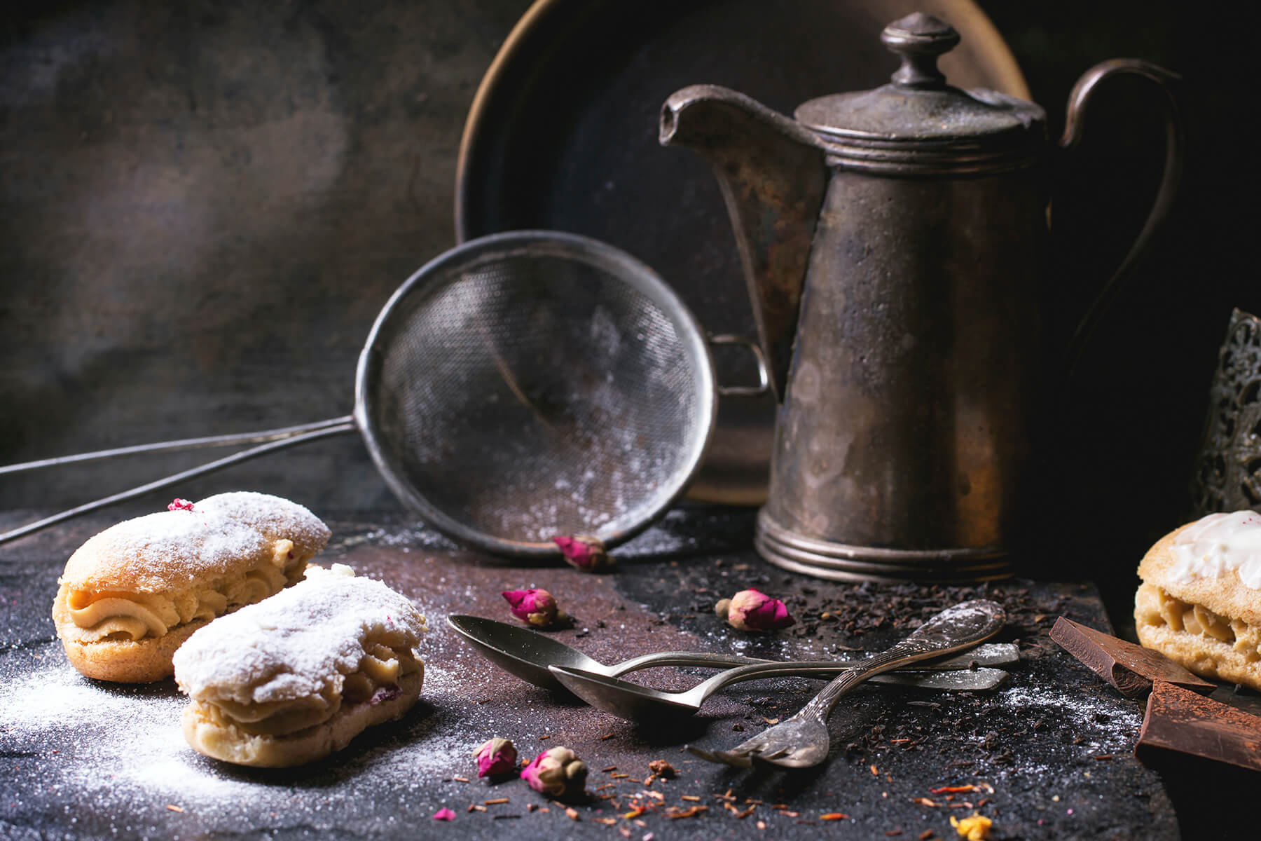 Mit Puderzucker bestäubte Éclairs in einem dunklen Stillleben mit Sieb und antiker Kaffeekanne