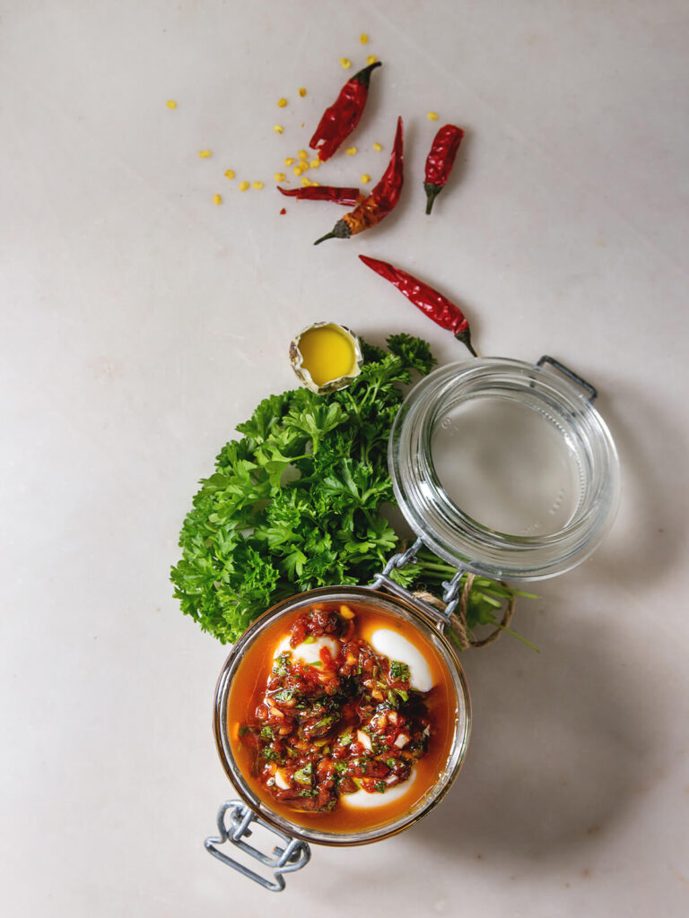 Eingelegte Wachteleier im Bügelglas mit roter Chili-Marinade, getrockneten Chilischoten und Petersilie