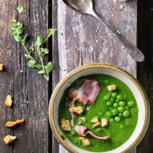 Cremige grüne Erbsensuppe in rustikaler Schale mit Speck und Croutons