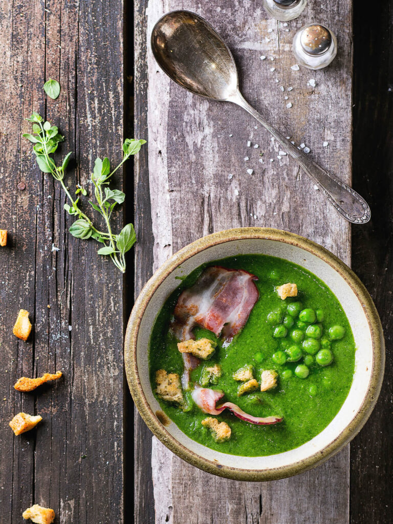 Cremige grüne Erbsensuppe in rustikaler Schale mit Speck und Croutons