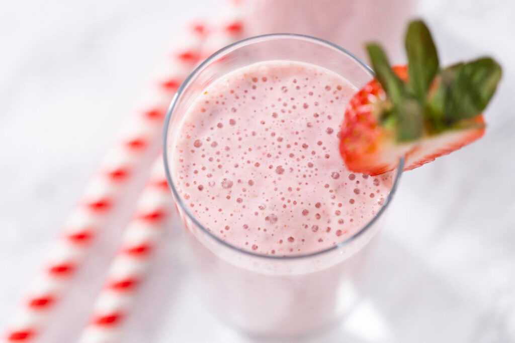 Erdbeer-Bananen-Power-Smoothie im hohen Glas mit Erdbeer-Garnitur und rot-weiß gestreiftem Strohhalm