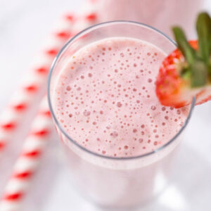 Erdbeer-Bananen-Power-Smoothie im hohen Glas mit Erdbeer-Garnitur und rot-weiß gestreiftem Strohhalm