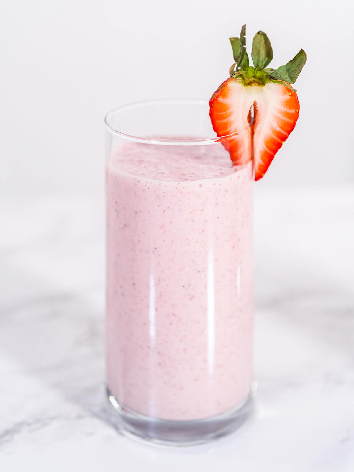 Zwei hohe Gläser Erdbeer-Bananen-Power-Smoothie in leuchtendem Rosa, jeweils mit rot-weiß gestreiftem Strohhalm und halbierter frischer Erdbeere am Rand