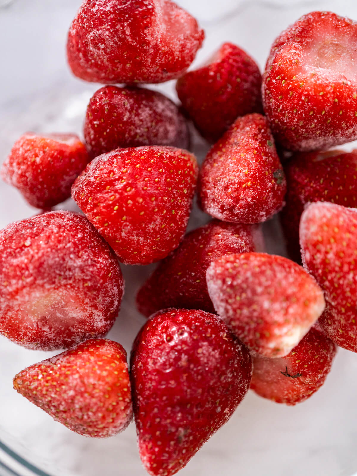 Tiefgefrorene Erdbeeren mit Reifkristallen in einer Glasschüssel, von oben fotografiert