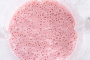Fertig pürierter Erdbeer-Bananen-Smoothie im Mixbecher von oben, dichte rosafarbene Masse mit feinen Bläschen