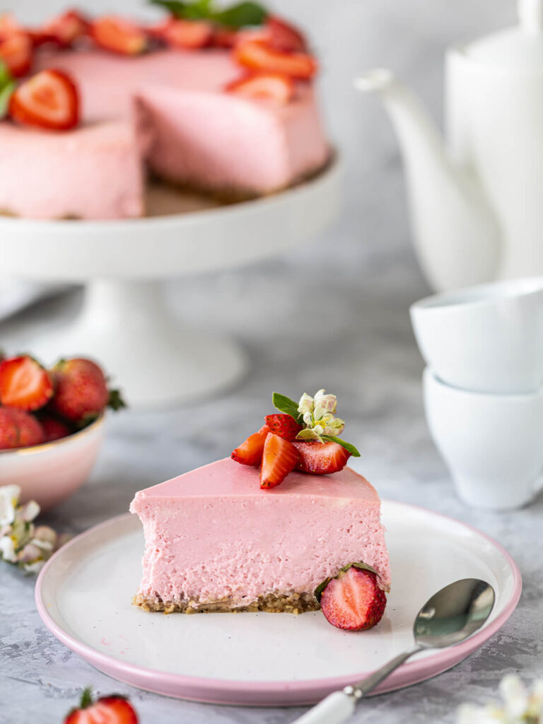 Anschnitt eines rosa No-Bake-Erdbeer-Cheesecakes mit halbierten Erdbeeren und weißer Blüte