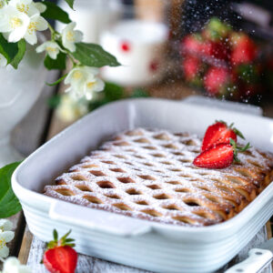 Erdbeer-Gitterkuchen mit geflochtenem Hefeteig-Gitter in weißer Auflaufform, mit Puderzucker bestäubt