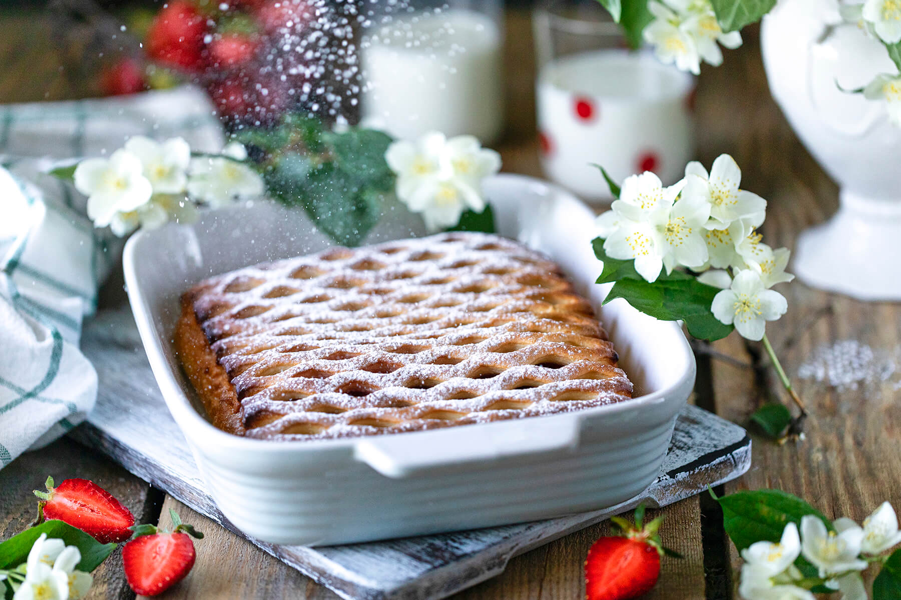 Erdbeer-Gitterkuchen mit geflochtenem Hefeteig-Gitter in weißer Auflaufform, mit Puderzucker bestäubt