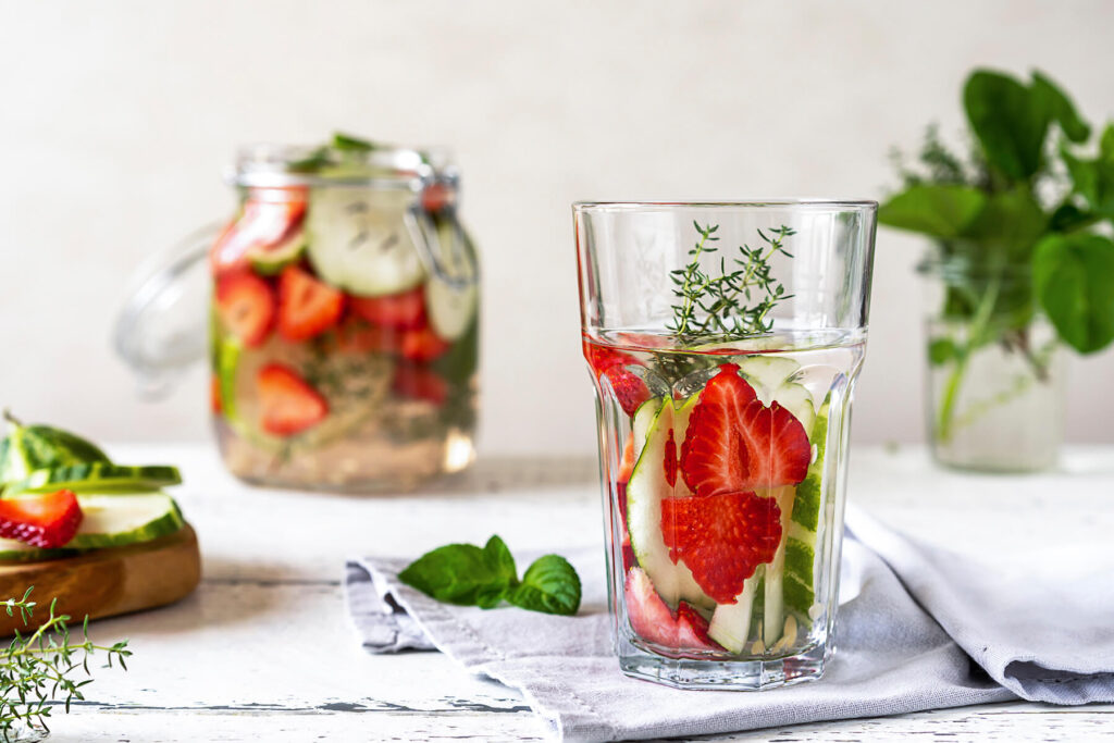 Erdbeer-Gurken-Infused-Water mit frischen Kräutern in Glaskaraffe