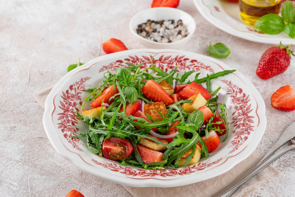 Erdbeer-Halloumi-Salat mit Rucola, roten Tomaten, roter Zwiebel und Basilikum auf dekoriertem Teller