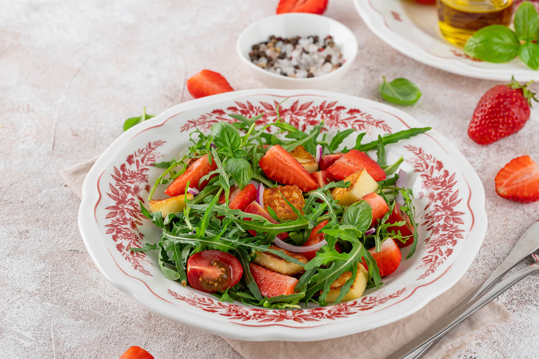 Erdbeer-Halloumi-Salat mit Rucola, roten Tomaten, roter Zwiebel und Basilikum auf dekoriertem Teller