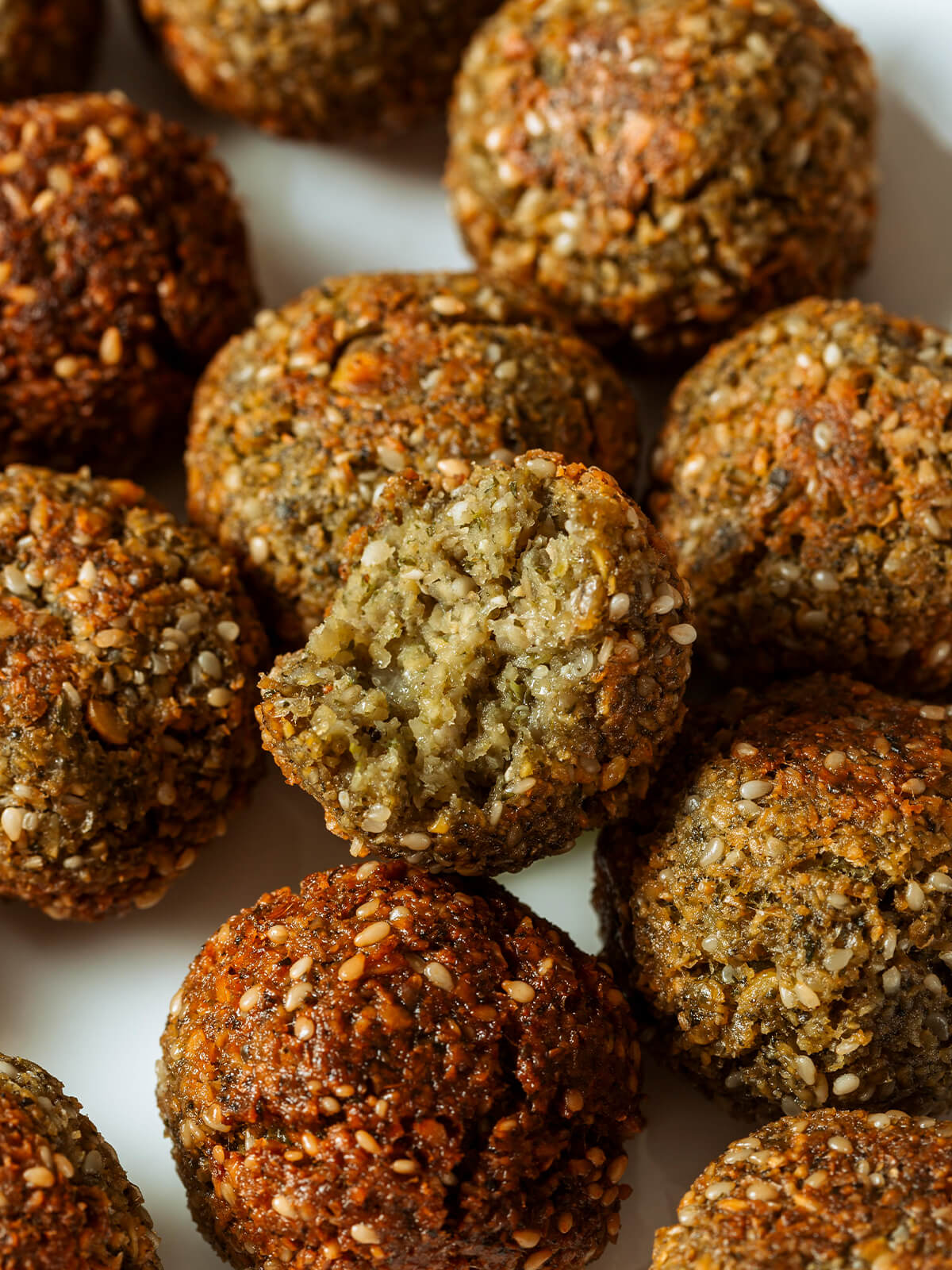 Aufgebrochene Falafel mit hellbeigem, krümeligem Kern und grünen Kräuterflecken unter der Sesamkruste
