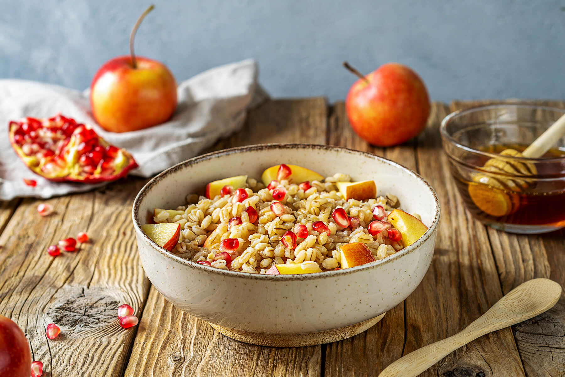 Schale mit cremigem Gerstenbrei aus Perlgraupen, Apfelwürfeln und Granatapfel-Kernen auf rustikalem Holztisch