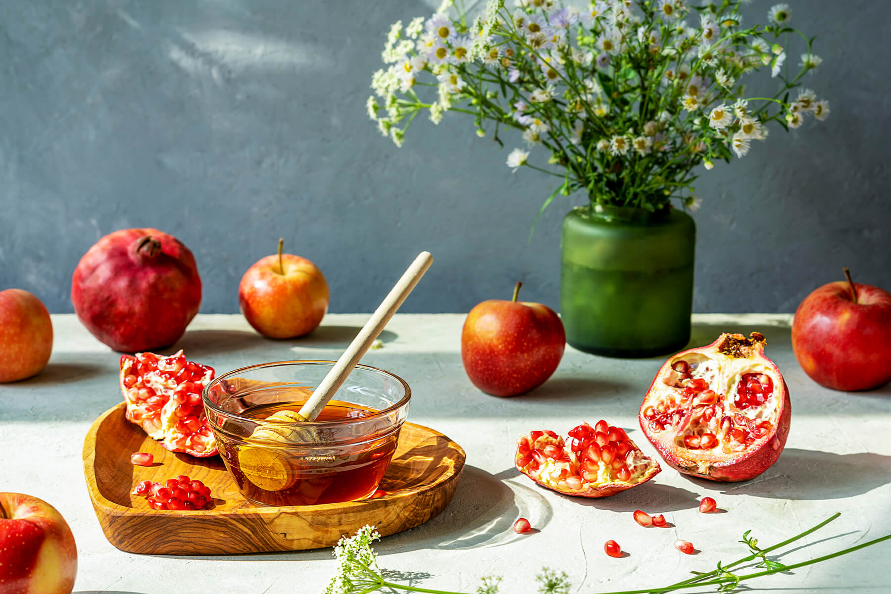 Ganze und halbierte Granatäpfel, rote Äpfel und ein Honigschälchen mit Holzlöffel als Symbole der Neujahrstafel