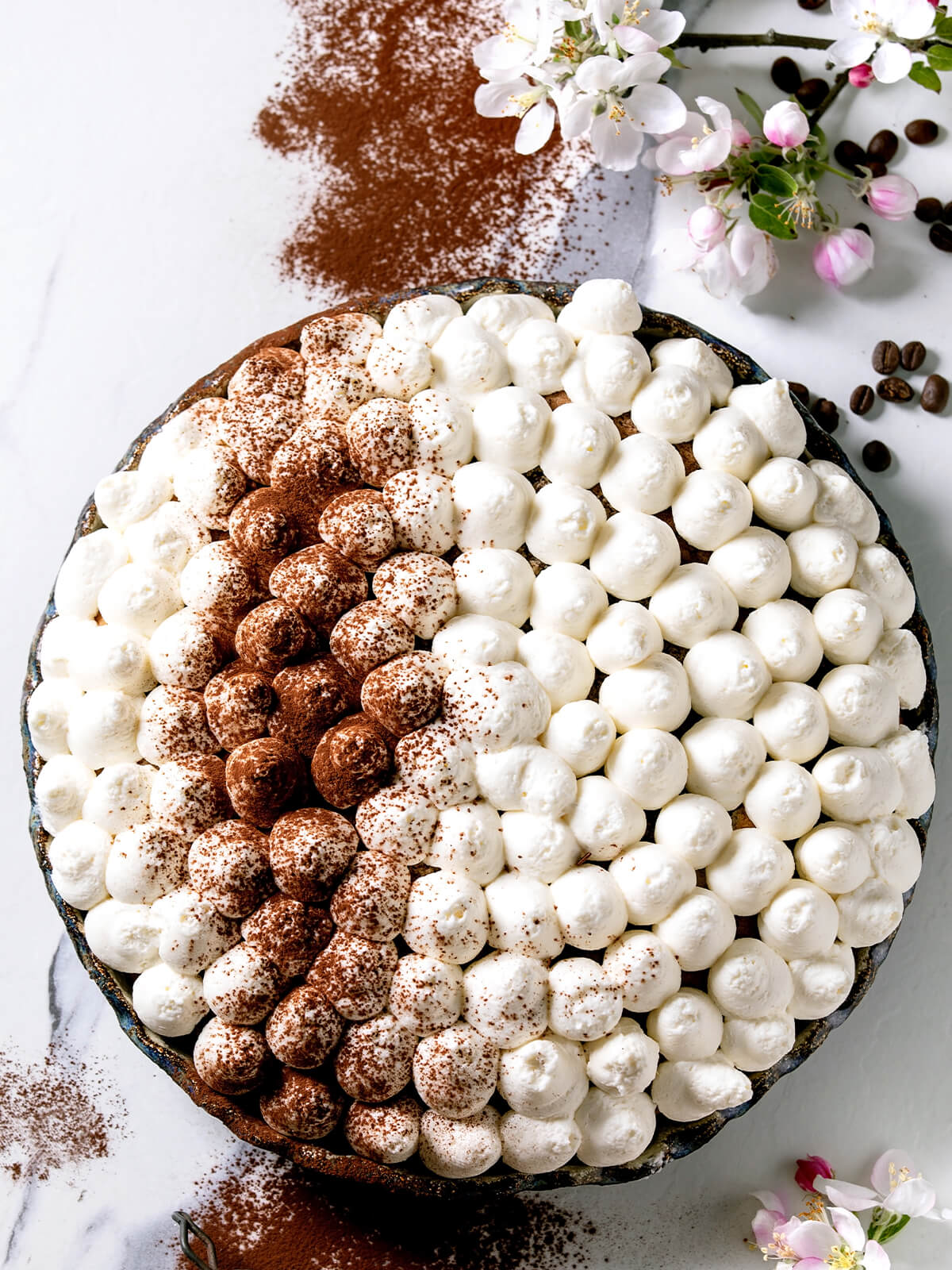 Glutenfreie Tiramisu-Torte von oben mit hellen Sahnetupfen und einem kakaobestäubten Streifen