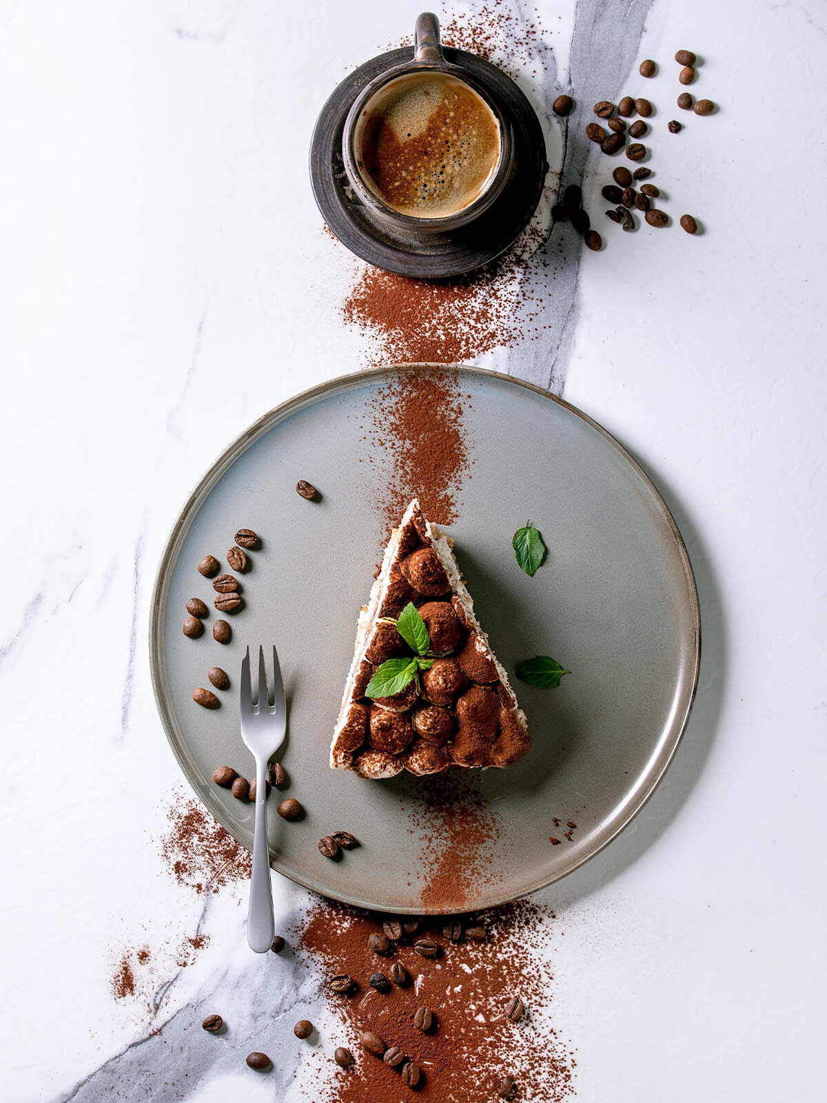 Ein Stück glutenfreie Tiramisu-Torte von oben auf grauem Teller mit Minze und Kakao