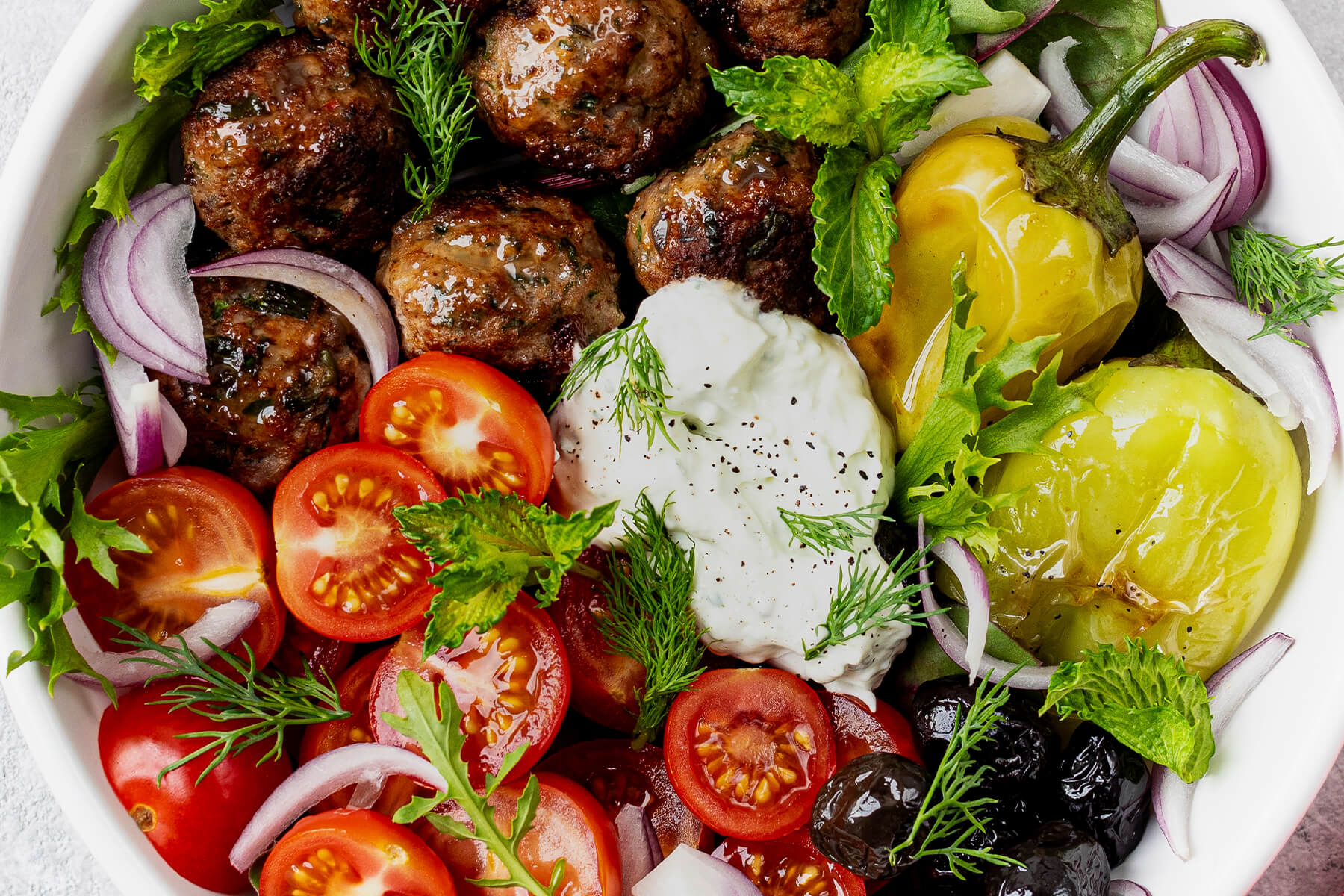 Nahaufnahme der Keftedes-Bowl mit Tzatziki, Frikadellen, Tomaten und Minze