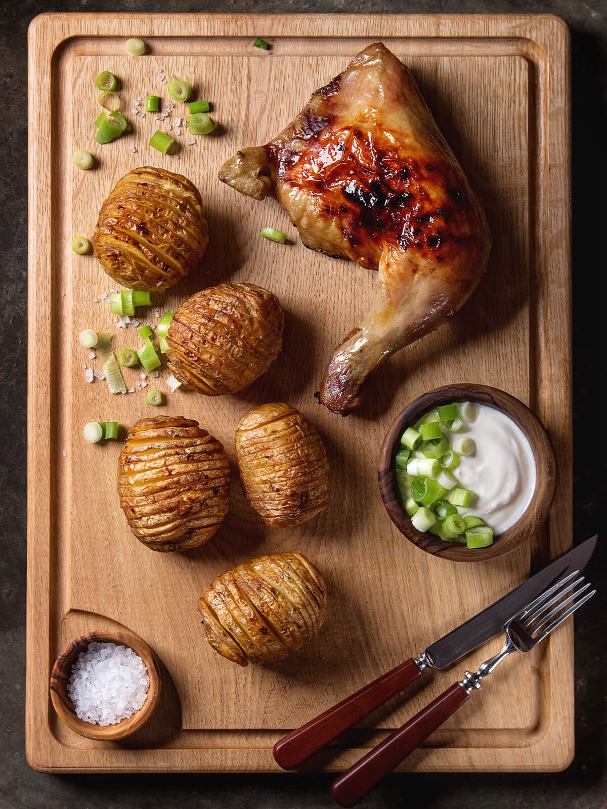 Hasselback-Kartoffeln auf Holzbrett mit glasierter Haehnchenkeule, Sauerrahm-Dip und Meersalzflocken