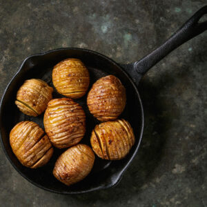 Sieben Hasselback-Kartoffeln dicht an dicht in kleiner gusseiserner Pfanne aus dem Ofen