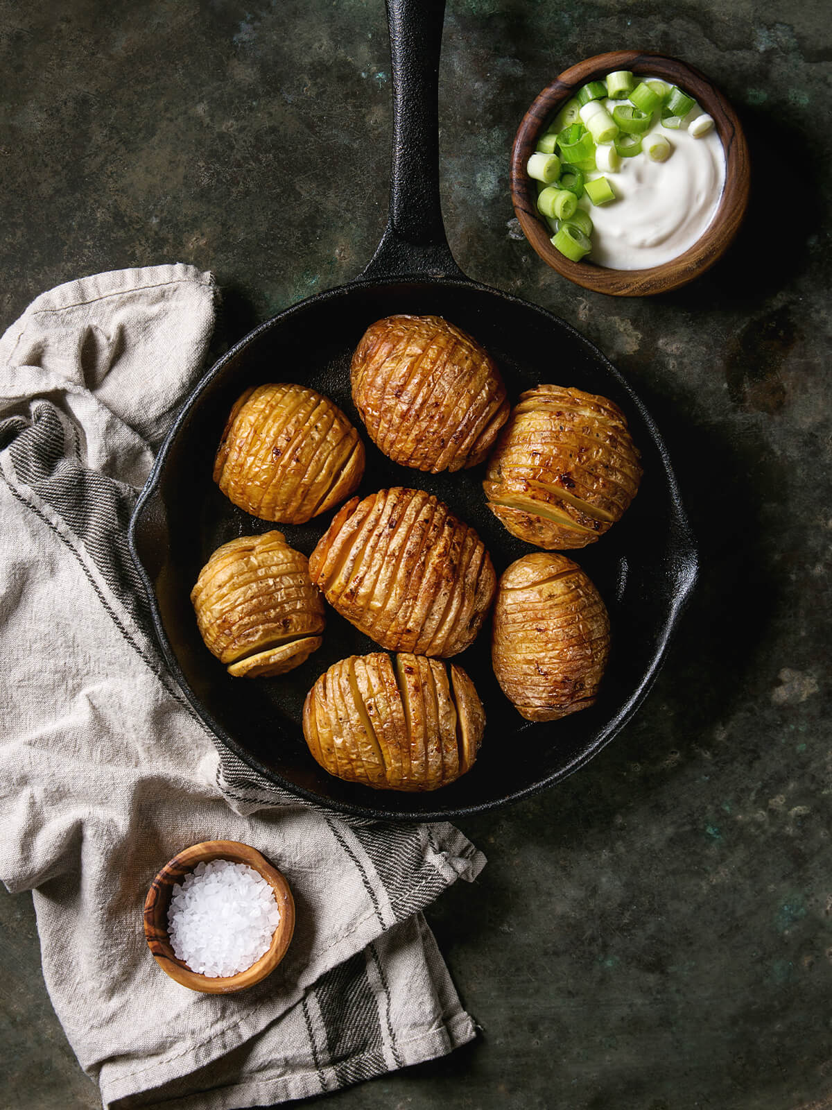 Hasselback-Kartoffeln dicht an dicht in kleiner gusseiserner Pfanne mit Sauerrahm-Dip und Meersalzflocken