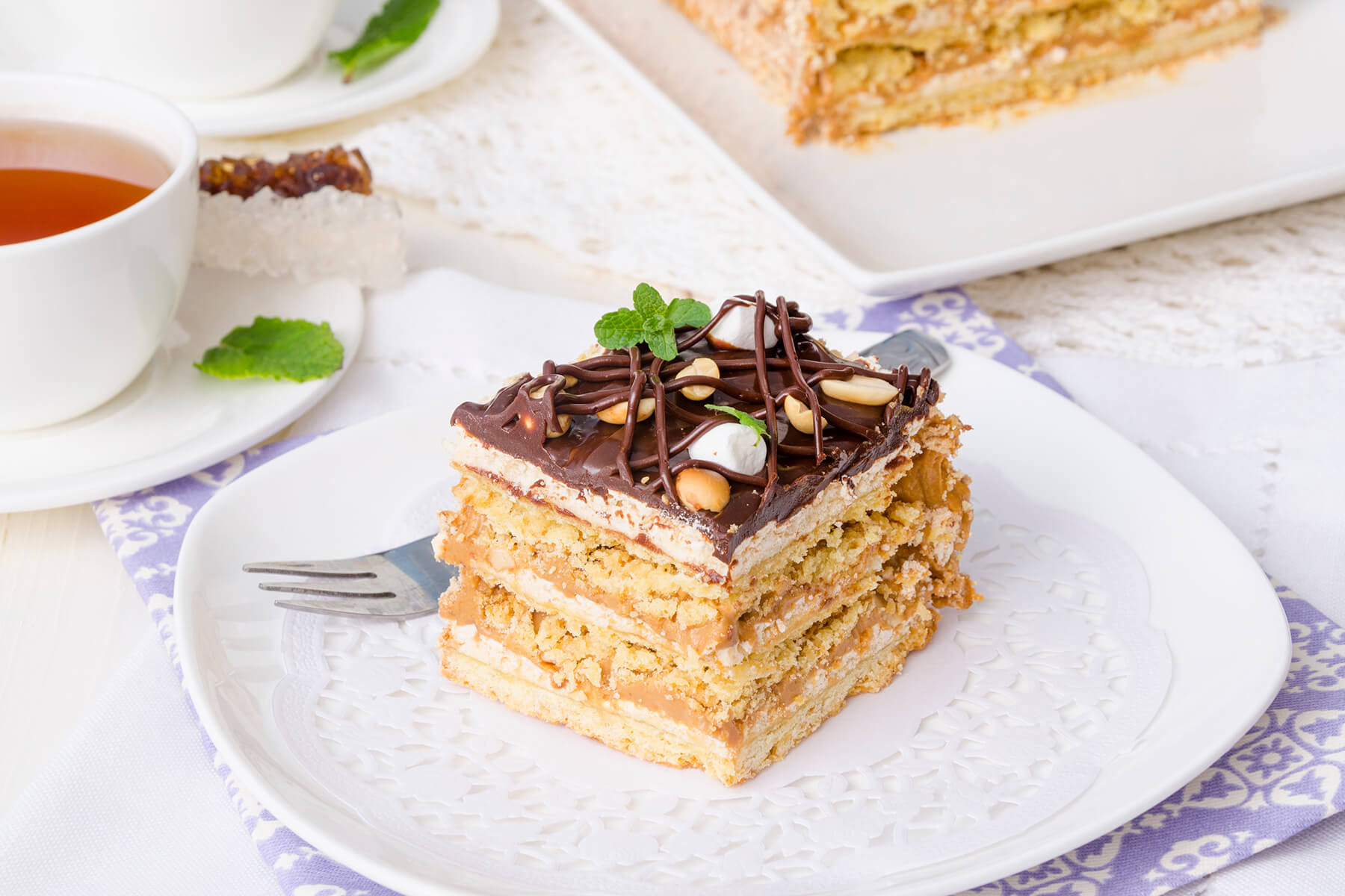 Angeschnittenes Stück Karamell-Erdnuss-Schichttorte mit sichtbaren Nussböden und Karamellcreme
