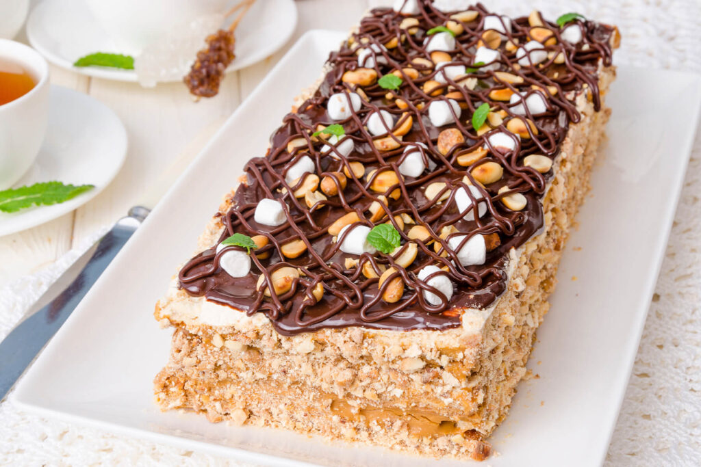Karamell-Sahne-Torte mit Meringue, gerösteten Erdnüssen und dunkler Schoko-Glasur