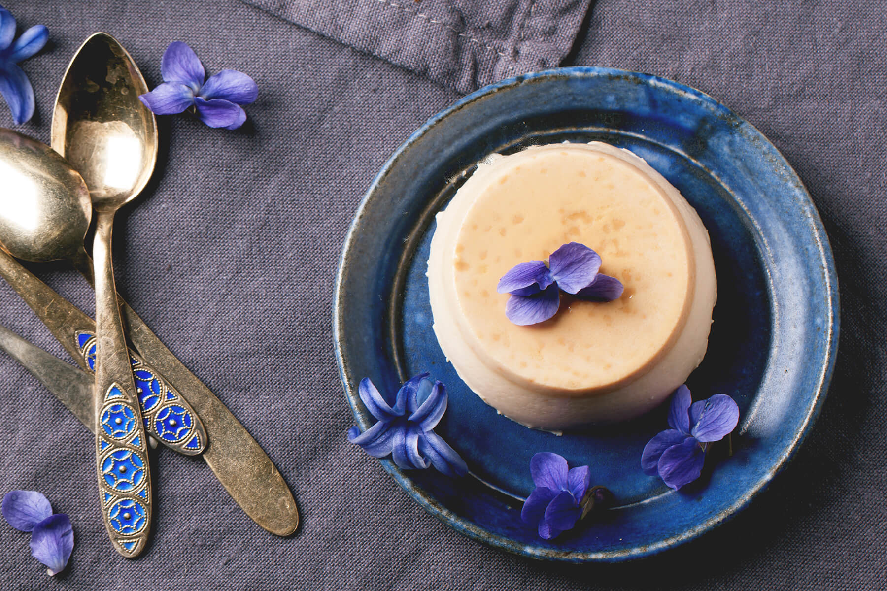Gestürzte Karamell-Panna-Cotta auf blauem Keramikteller mit frischen Veilchen-Blüten