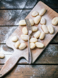 Rohe Kartoffel-Gnocchi mit Gabelrillen auf einem bemehlten Holzbrett neben einer Gabel