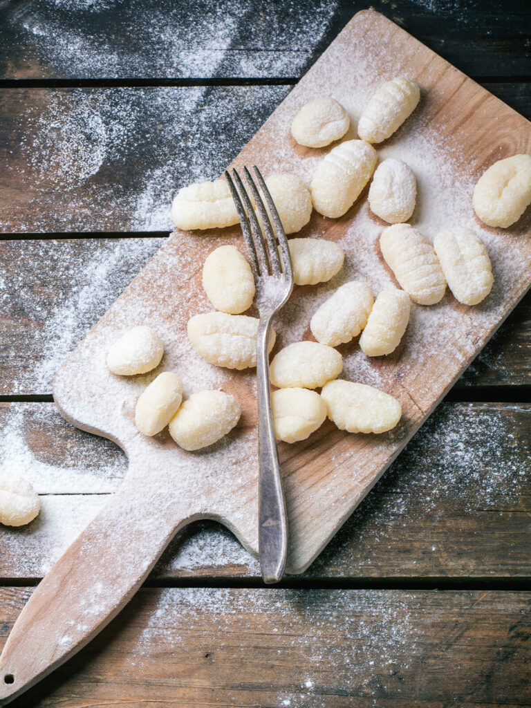 Rohe Kartoffel-Gnocchi mit Gabelrillen auf einem bemehlten Holzbrett neben einer Gabel