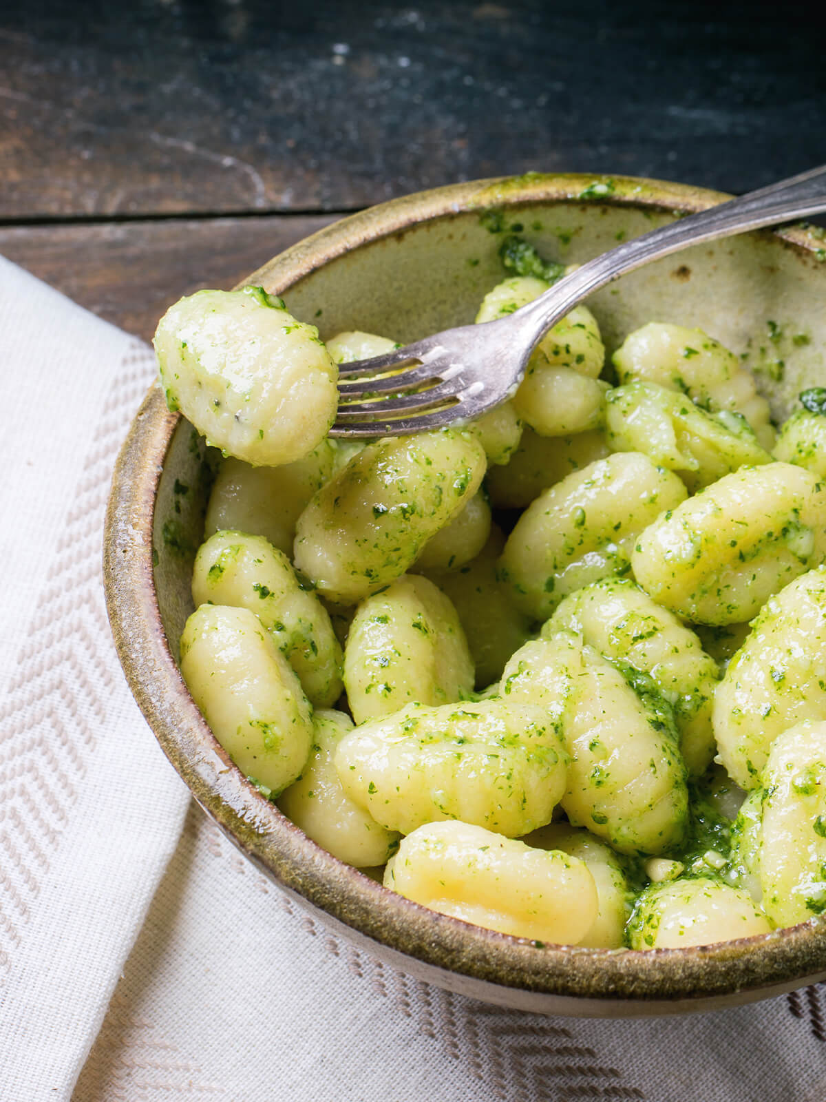 Kartoffel-Gnocchi mit Basilikum-Pesto in einer rustikalen Keramikschale mit Gabel