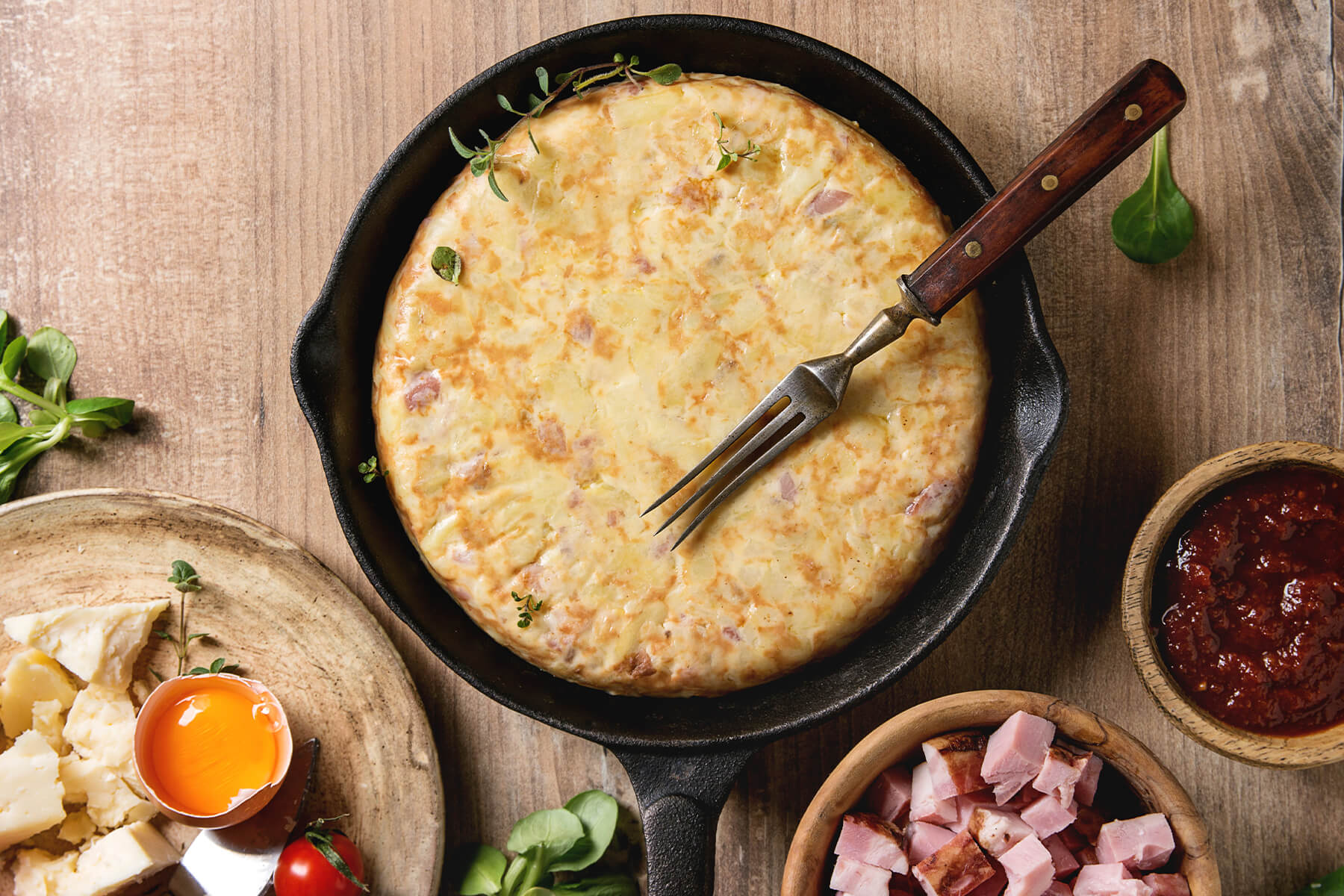 Goldene Kartoffel-Tortilla mit Speck und geschmolzenem Käse in der Gusspfanne mit Holzgriff-Gabel
