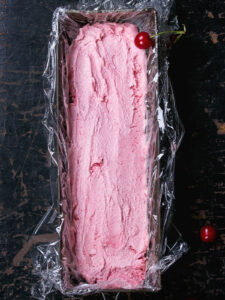 Cremig-rosa Kirsch-Sorbet in einer mit Folie ausgelegten Kasten-Form vor dem Portionieren