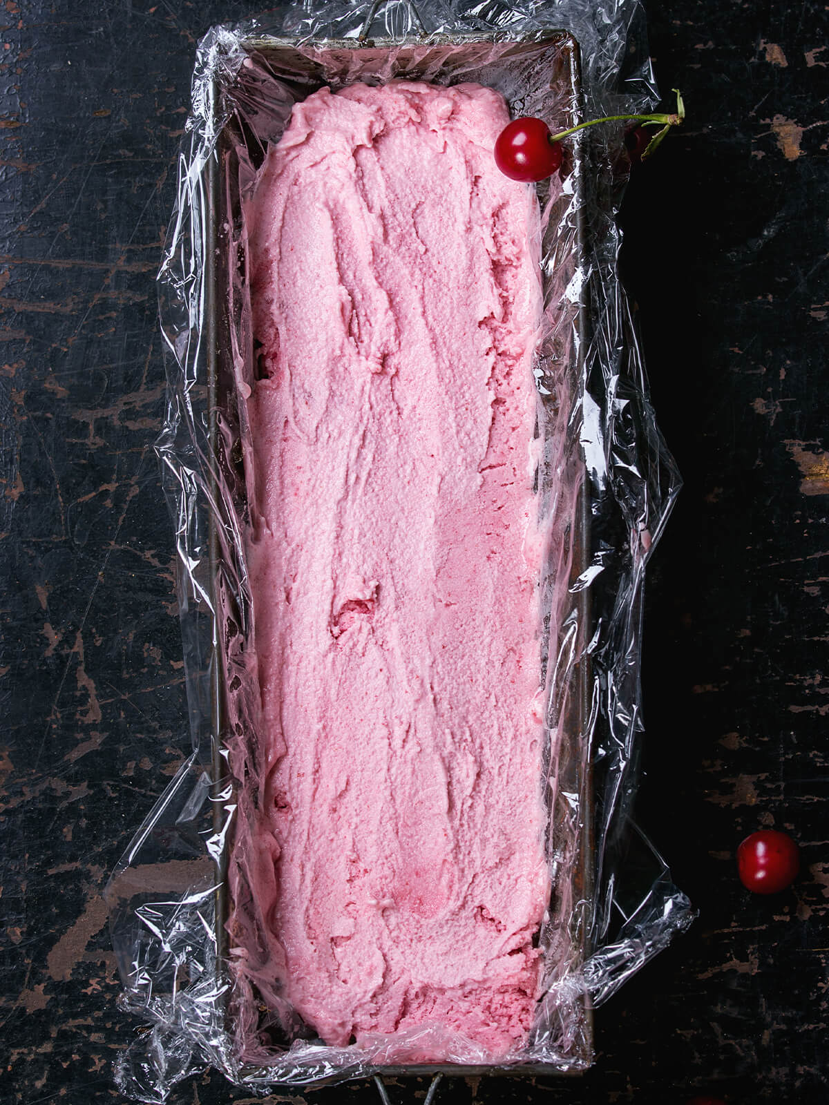 Cremig-rosa Kirsch-Sorbet in einer mit Folie ausgelegten Kasten-Form vor dem Portionieren