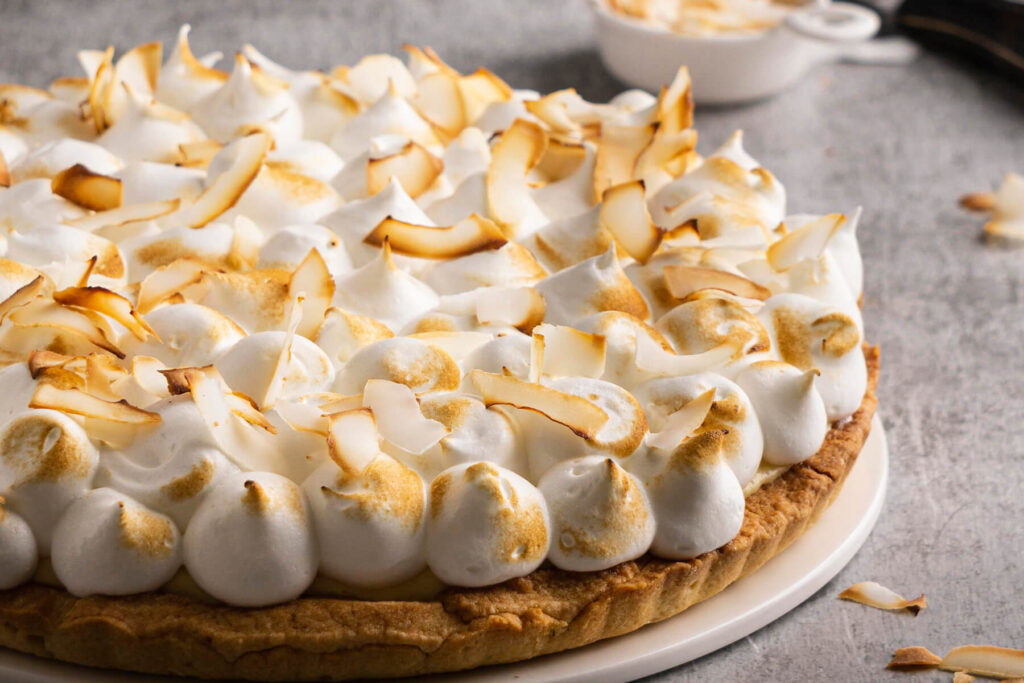 Ganze Kokos-Sahne-Tarte mit goldgebackener Baiser-Haube und gerösteten Kokosflocken