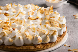 Ganze Kokos-Sahne-Tarte mit goldgebackener Baiser-Haube und gerösteten Kokosflocken