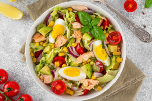 Lachs-Avocado-Salat mit Eiern, Mais und Tomaten auf rundem Teller