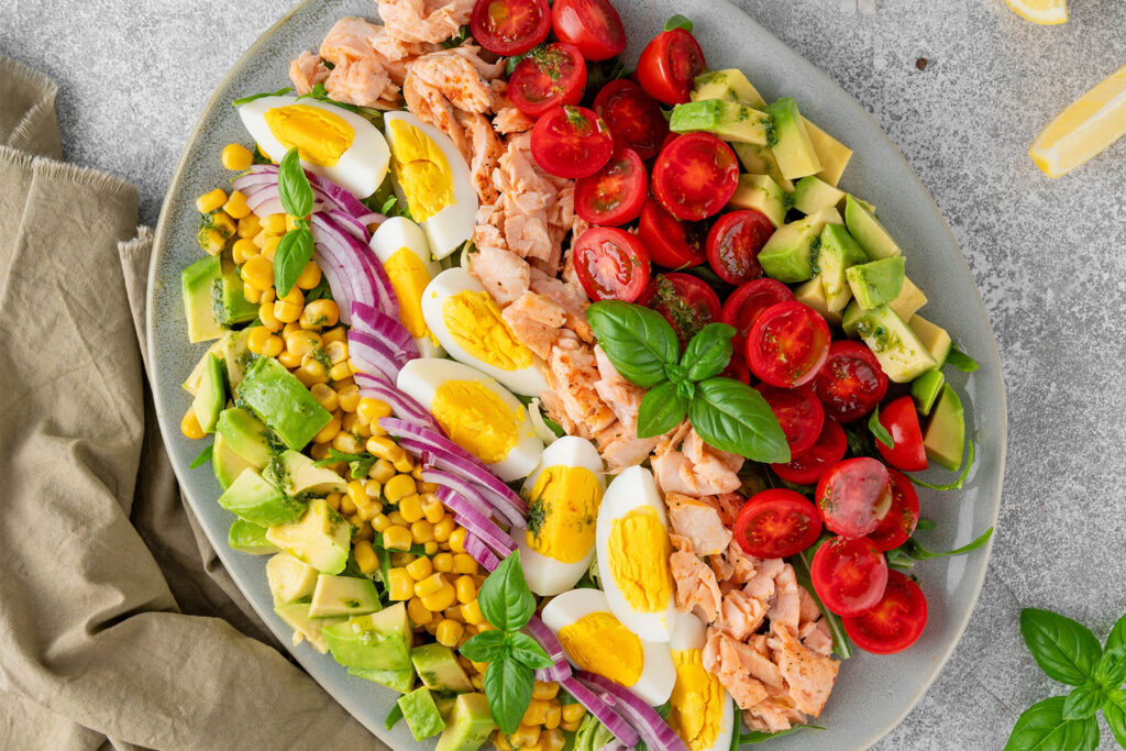 Lachs-Avocado-Cobb-Salat in Reihen angerichtet mit Mais, Avocado, Eiern und Tomaten