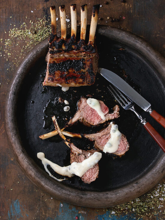 Gegrilltes Lammkarree mit dunkler Kruste, in Koteletts geschnitten mit rosa Mitte, nach Wunsch mit cremiger Kräutersauce