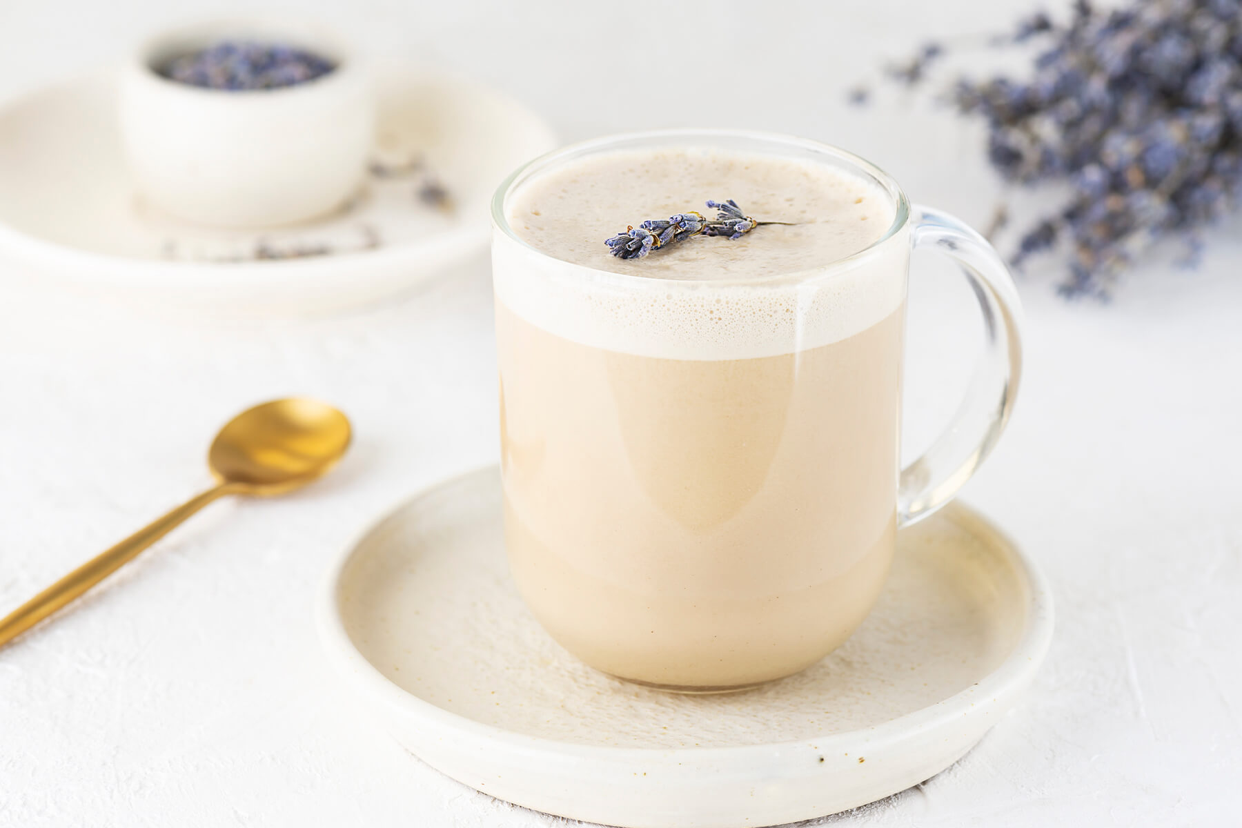 Cremiger naturbeiger Lavendel-Latte im Glasbecher mit feiner Mousse-Krone und Lavendelzweig