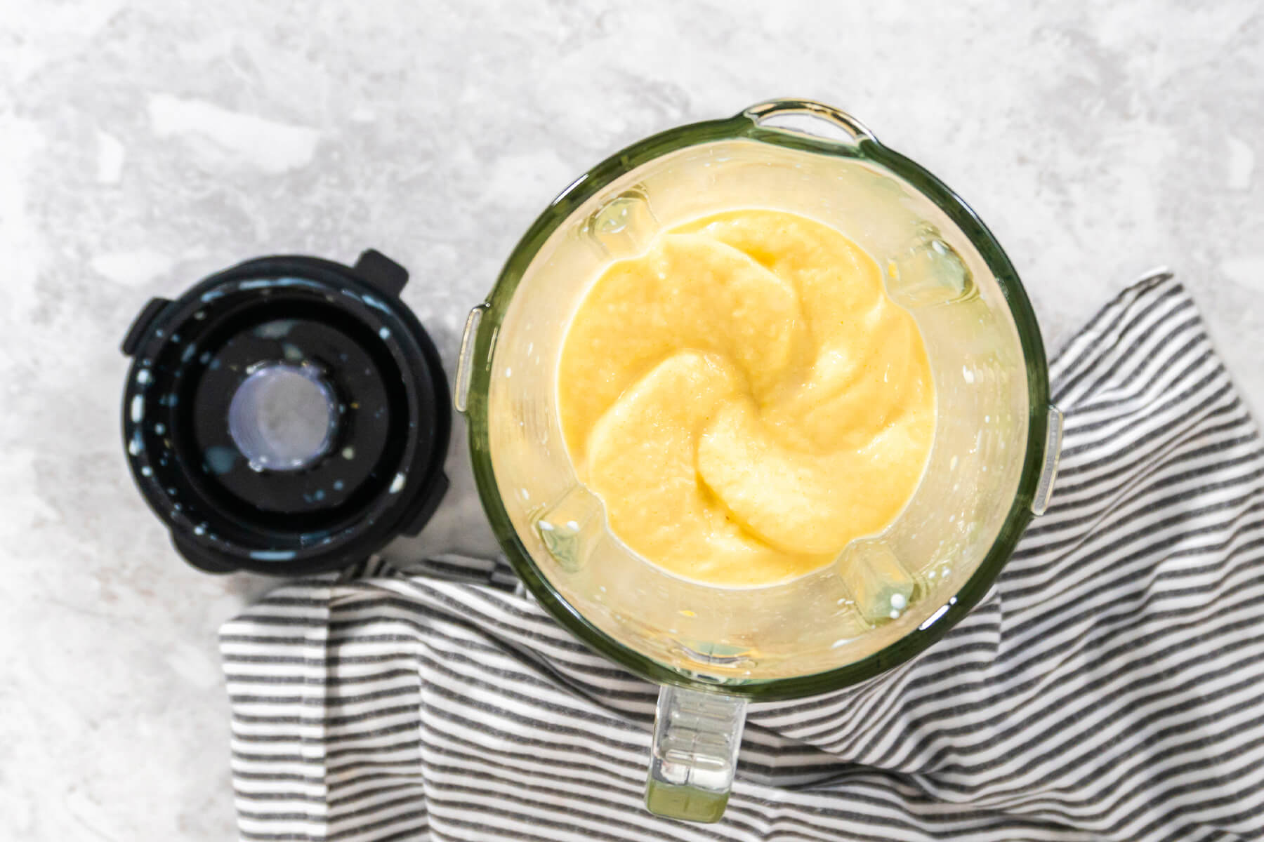 Fertig pürierter goldgelber Mango-Smoothie von oben im Standmixer, daneben der Deckel
